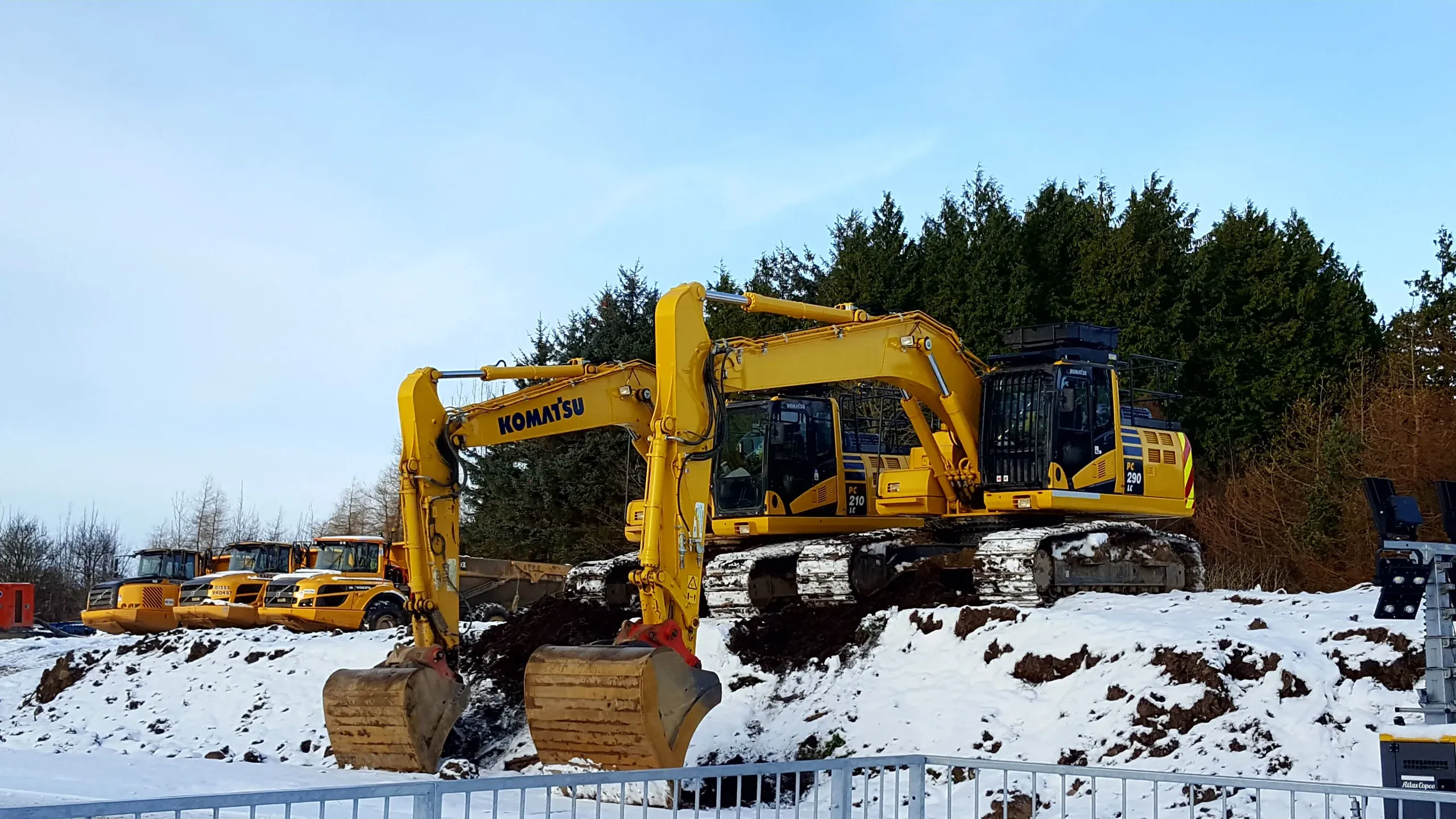 Two excavators parked in snow beside a treeline