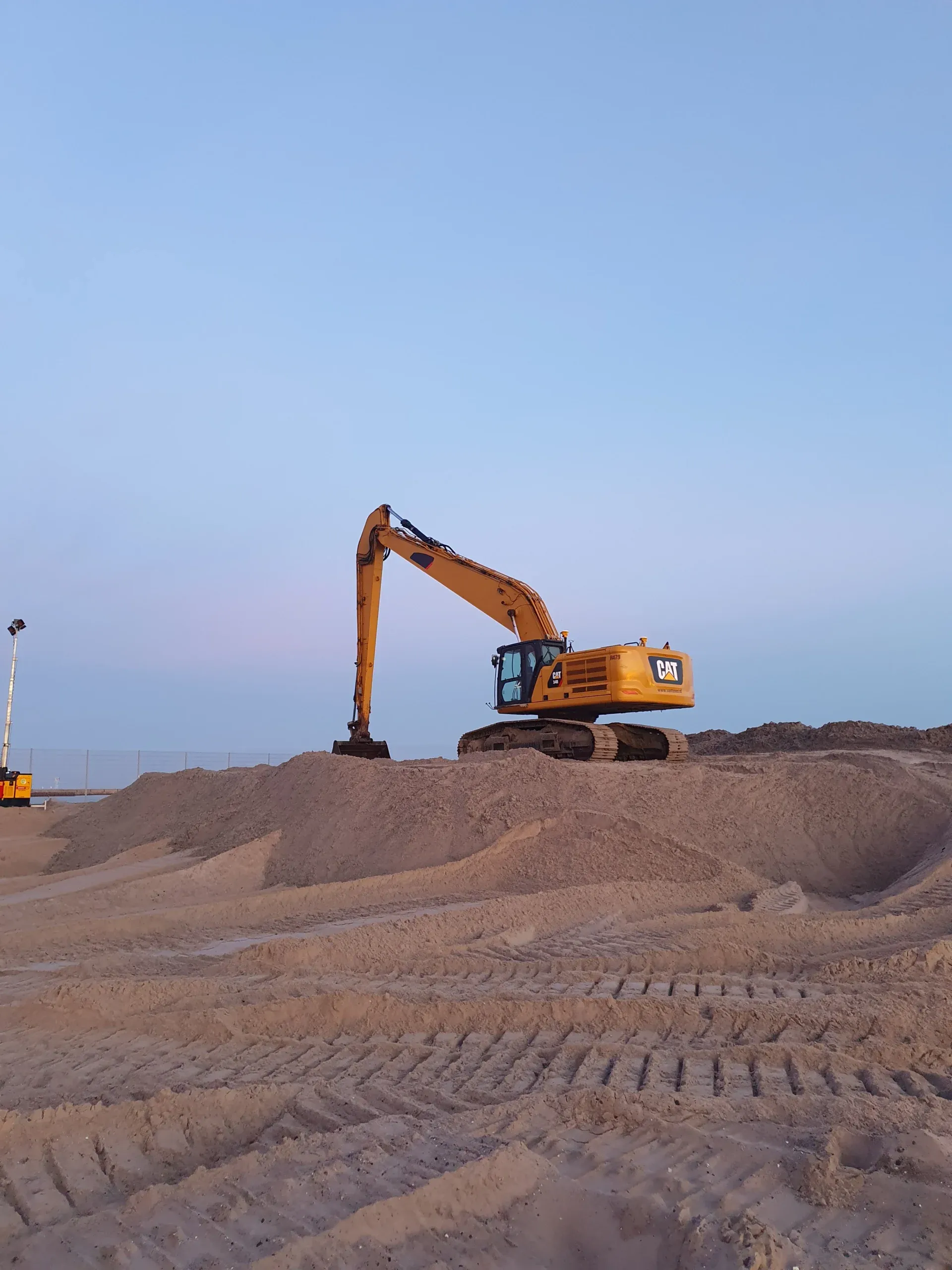 A long-reach excavator on a sand bank at dusk