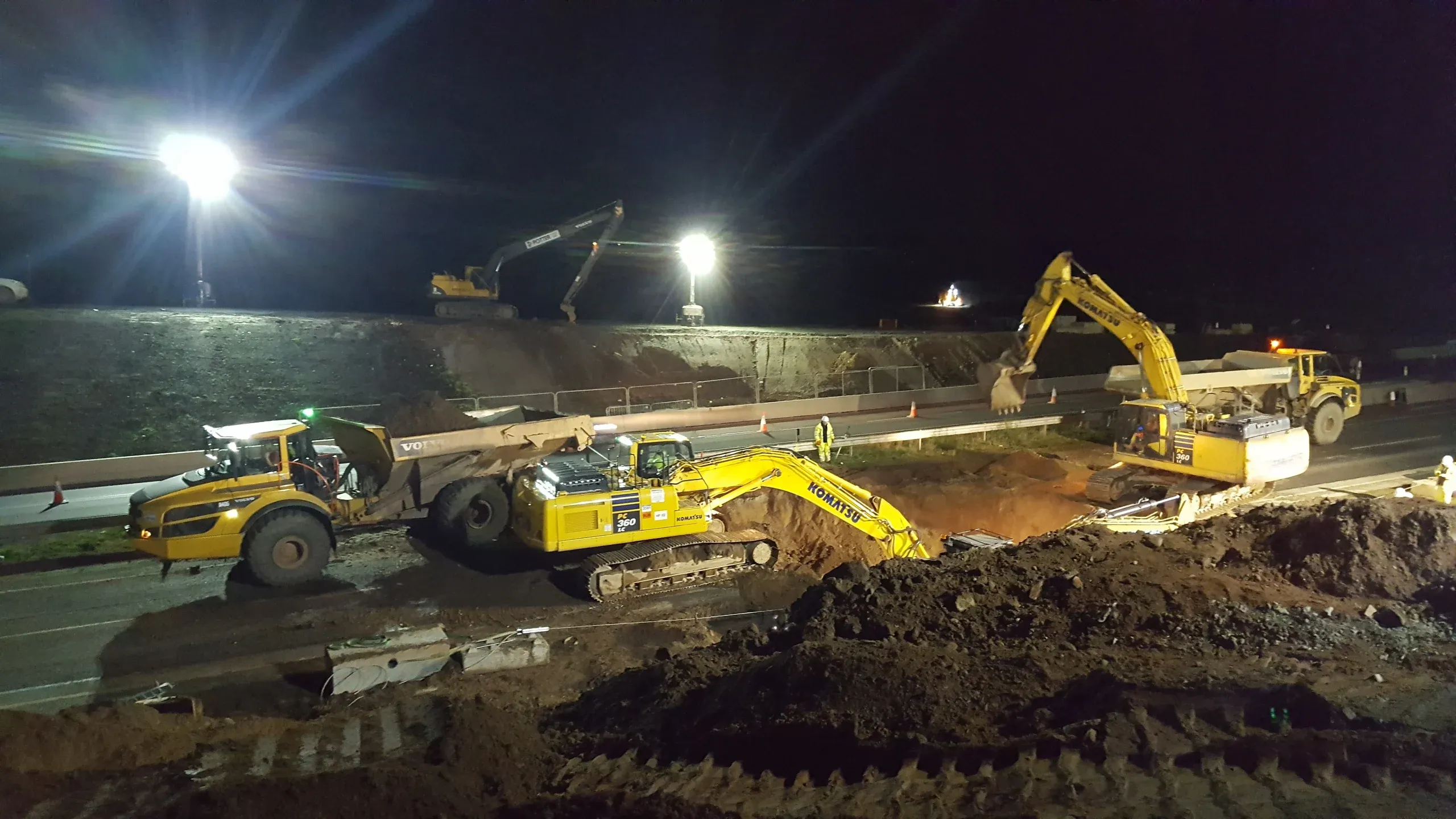 Excavators and a dumper working under floodlights at night